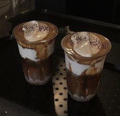 two glasses of iced coffee sitting on top of a black table next to each other