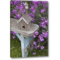 a bird house sitting on top of a wooden bench in front of purple wildflowers