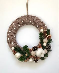 a christmas wreath with pine cones and white balls hanging from a string on a wall