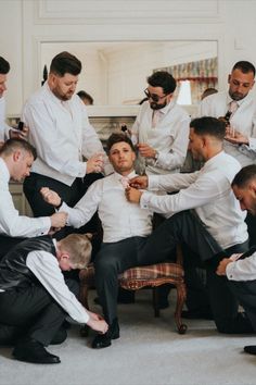 a group of men standing around each other tying their ties in a room with white walls