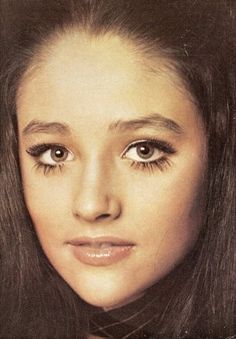 an old photo of a woman with long brown hair and big blue eyes, looking directly into the camera