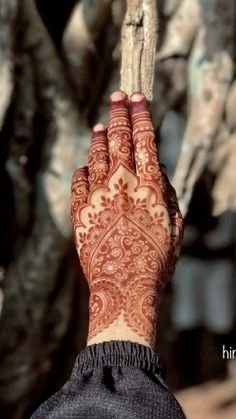 a woman's hand with henna on it holding a stick in front of some trees