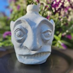 a white ceramic face sitting on top of a table next to purple and white flowers