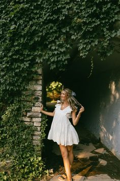 a woman standing in front of a wall covered in vines and ivys with her arms outstretched