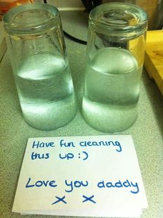 two glass jars with water in them sitting on a counter next to a sign that says, have fun cleaning this up i love you daddy