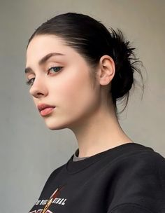 a woman with black hair and blue eyes is wearing a black t - shirt that has an image of a bird on it