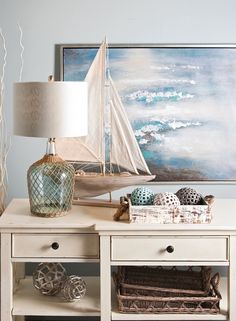 a white table topped with a lamp next to a painting and basket filled with balls