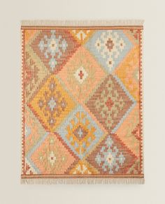 an orange, yellow and blue rug with fringes on the bottom is shown in front of a white wall