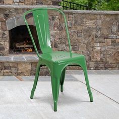 a green metal chair sitting in front of a fire place with a brick wall behind it