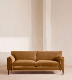 a tan couch sitting on top of a hard wood floor next to a white wall