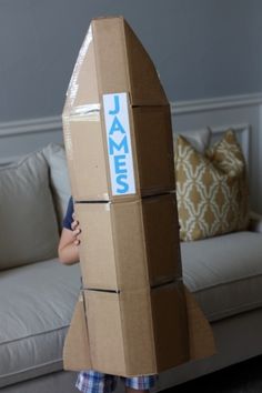 a young boy standing in front of a cardboard rocket ship with the name james on it