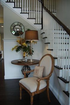 a chair sitting under a stair case next to a table with a lamp on it