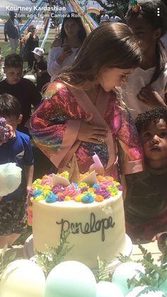 a woman standing in front of a cake with candles on it and children around her