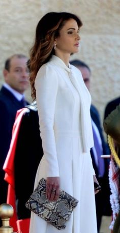 a woman in a white dress and jacket holding a snake skin purse while standing next to other people