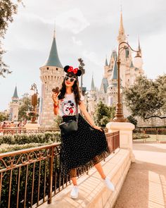 a woman standing in front of a castle with minnie mouse on her shirt and skirt