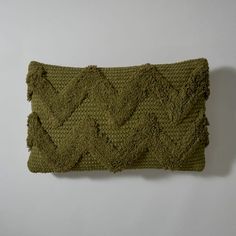 a green knitted pillow sitting on top of a white wall