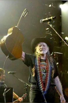 a man with long hair wearing a black hat and holding a guitar in his right hand