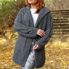 a woman standing in the woods with her hands on her hips wearing a gray knitted cardigan