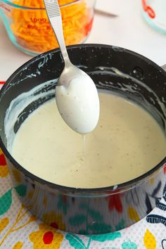 a spoon is being used to dip cheese into a sauce in a pot on the table