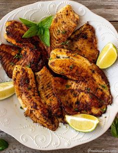 grilled chicken on a white plate with lemon wedges and mint garnish