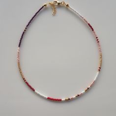 a beaded necklace on a white surface with a gold clasp and red, white, and blue beads