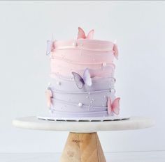 a multi layer cake with pink and purple frosting on a white plate next to a wooden stand