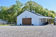 a white barn with two garages in front of it and lots of trees around