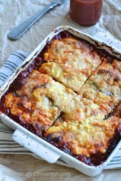 a casserole dish with cheese and sauce in it on a table next to a spoon