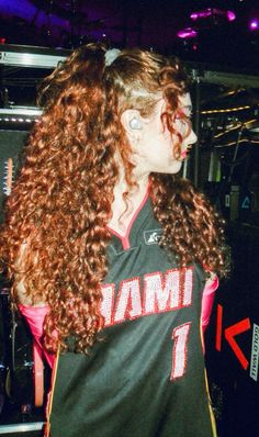 a woman with long curly hair wearing a jersey