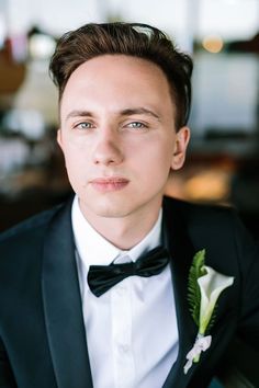 a young man in a tuxedo looks at the camera while wearing a boutonniere