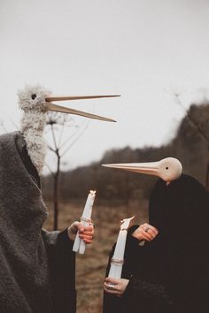 two people with long beaks holding candles in front of their faces and one has a bird's head on it