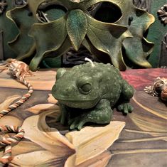 a green frog figurine sitting on top of a table next to some leaves