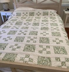 a bed with a green and white quilt on it's headboard next to a night stand