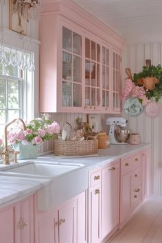 a kitchen with pink cabinets and flowers in the window sill, along with white counter tops