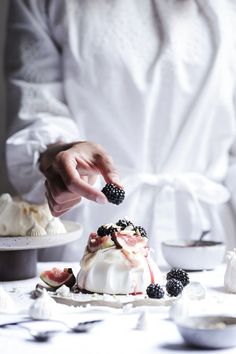 a woman is decorating a cake with berries and whipped cream