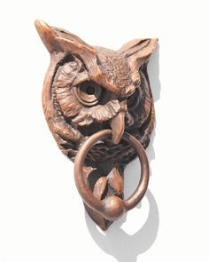 an owl door knockle with a ring on it's side, hanging from the wall