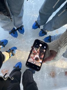 two people standing in the snow with their feet up and one person holding an iphone