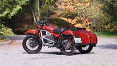 a red motorcycle parked on top of a gravel road next to trees and bushes in the background