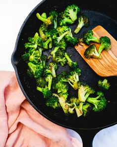 broccoli is being cooked in a skillet with a wooden spatula on the side