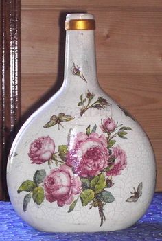 a white vase with pink roses painted on it sitting on a blue table cloth next to a wooden wall