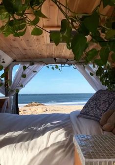 a bed sitting under a wooden roof next to the ocean on top of a sandy beach