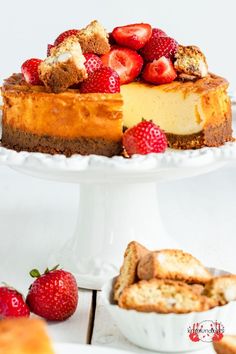 a cheesecake with strawberries is on a white cake platter next to other desserts