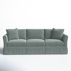 a couch with four pillows on it in front of a white wall and grey floor