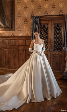 a woman in a white wedding dress standing on a wooden floor with her hands behind her back