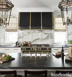 a kitchen with marble counter tops and gold accents on the stove top, along with hanging lights