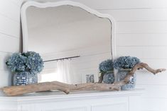 there is a mirror and vases on the mantel in this white room with blue hydrangeas