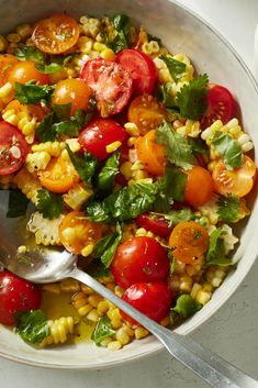 a white bowl filled with corn, tomatoes and green leafy garnishments