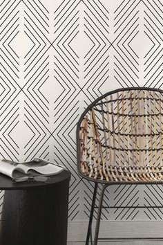 a rattan chair next to a black table with a magazine on it and a white wall behind it