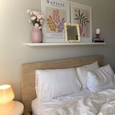 a bed with white sheets and pillows next to a pink vase on top of the headboard