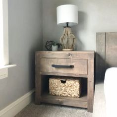 a nightstand with two baskets on it next to a lamp in a room that has gray walls and carpet